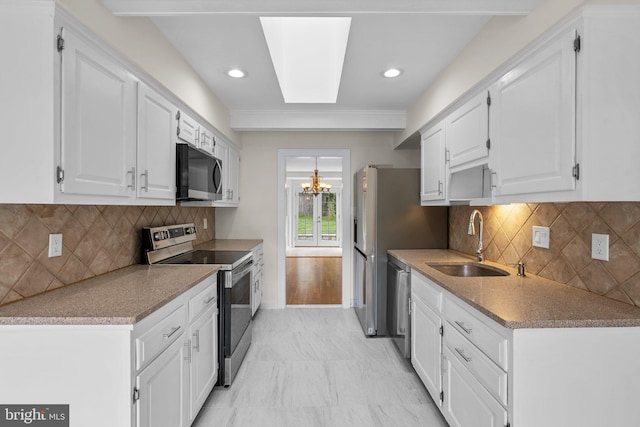 kitchen featuring appliances with stainless steel finishes, a chandelier, a sink, white cabinets, and decorative backsplash