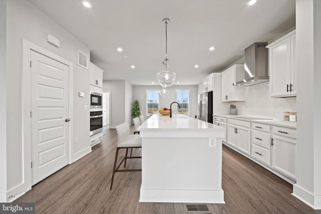 kitchen featuring a sink, visible vents, wall chimney exhaust hood, an island with sink, and appliances with stainless steel finishes