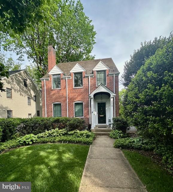 traditional-style home with brick siding, a chimney, and a front lawn