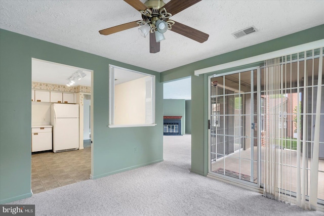 carpeted empty room featuring a ceiling fan, a textured ceiling, baseboards, visible vents, and rail lighting