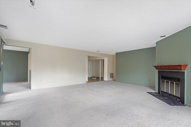 unfurnished living room with carpet flooring, a fireplace with flush hearth, and visible vents