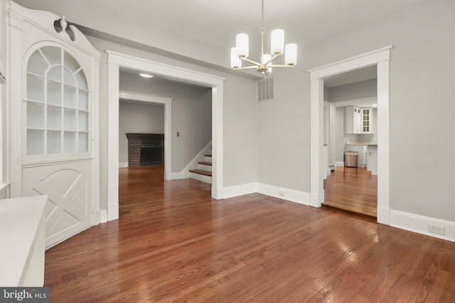 331 E Maple Rd, Linthicum Heights, MD 21090 - unfurnished dining area with a chandelier, stairs, wood finished floors, a brick fireplace, and baseboards