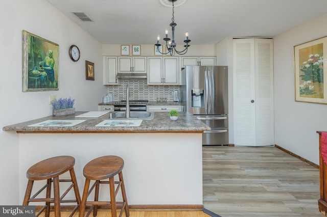 kitchen featuring stainless steel appliances, a peninsula, under cabinet range hood, light wood finished floors, and a chandelier
