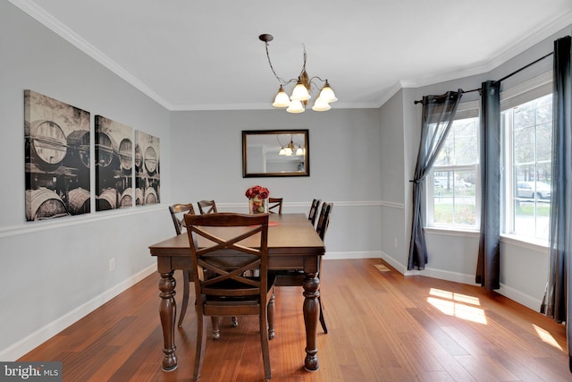 dining space with wood finished floors, baseboards, ornamental molding, and a notable chandelier