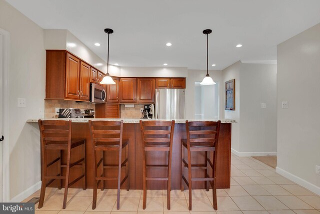kitchen featuring baseboards, a peninsula, brown cabinets, tasteful backsplash, and appliances with stainless steel finishes