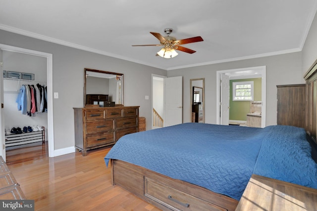 bedroom featuring baseboards, ensuite bathroom, ornamental molding, light wood finished floors, and a walk in closet