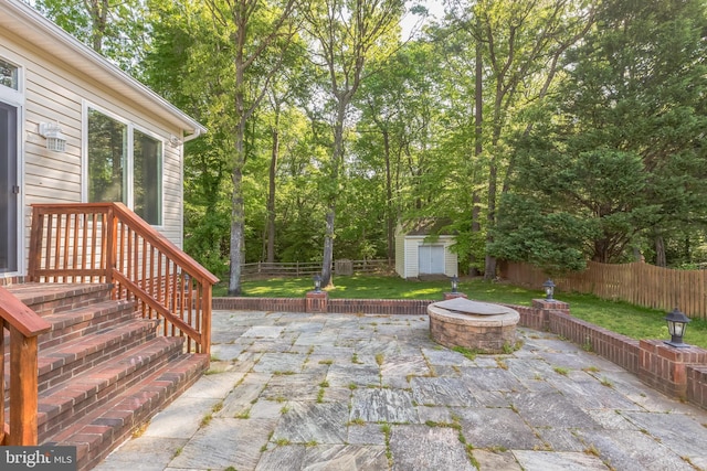 view of patio / terrace featuring an outdoor fire pit, an outdoor structure, a fenced backyard, and a storage unit