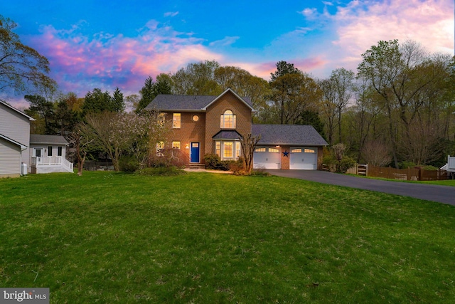 view of front of house featuring aphalt driveway, fence, an attached garage, brick siding, and a yard
