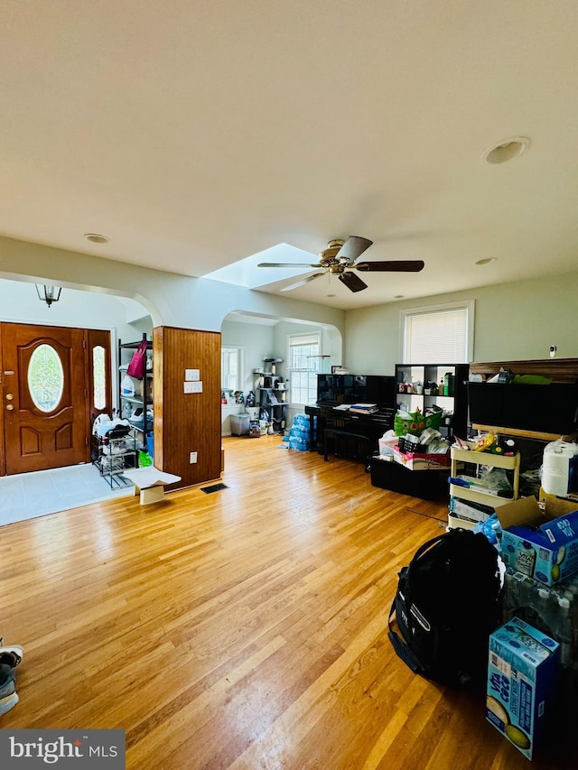 living room with arched walkways, ceiling fan, and light wood-type flooring