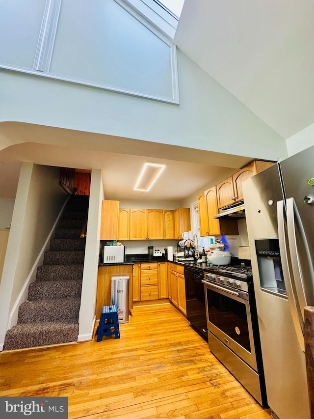 kitchen featuring appliances with stainless steel finishes, light wood-type flooring, high vaulted ceiling, dark countertops, and under cabinet range hood