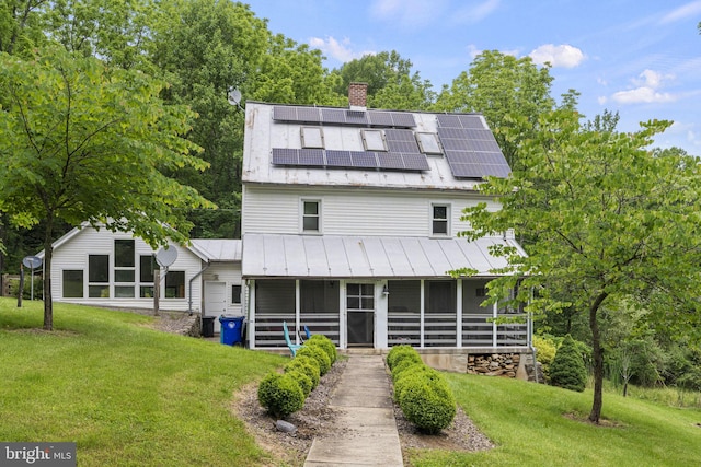 back of house featuring a yard, a chimney, a sunroom, and solar panels