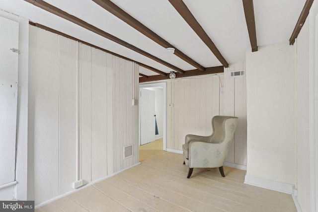 living area featuring light wood-style floors, wooden walls, beam ceiling, and visible vents