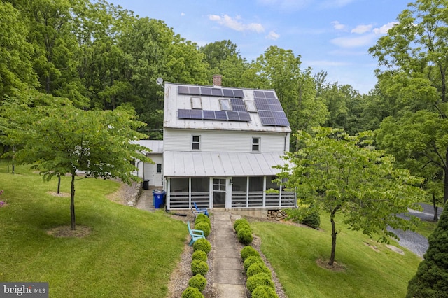 rear view of property with a lawn, a chimney, a sunroom, and roof mounted solar panels