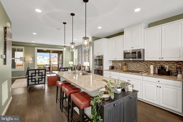 kitchen with appliances with stainless steel finishes, a sink, backsplash, an island with sink, and white cabinetry