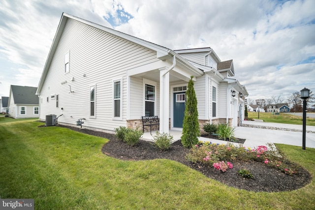 view of side of property with a yard, driveway, covered porch, an attached garage, and central AC