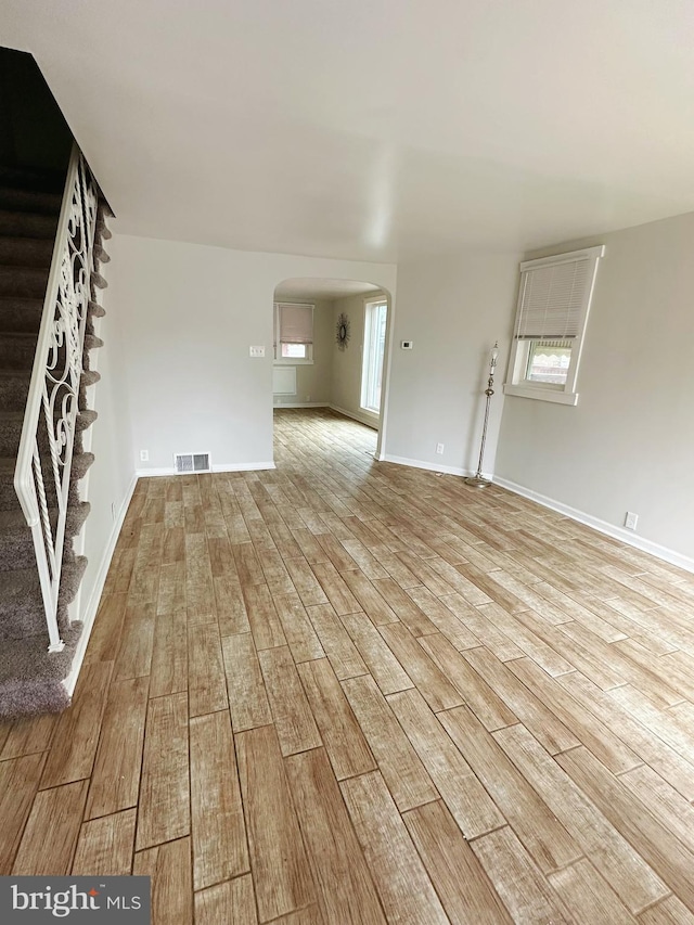 unfurnished living room featuring light wood-style floors, visible vents, arched walkways, and stairway