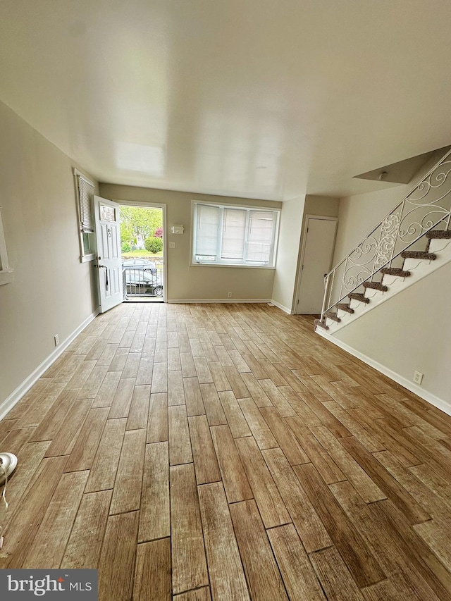 unfurnished living room with wood finished floors, baseboards, and stairs