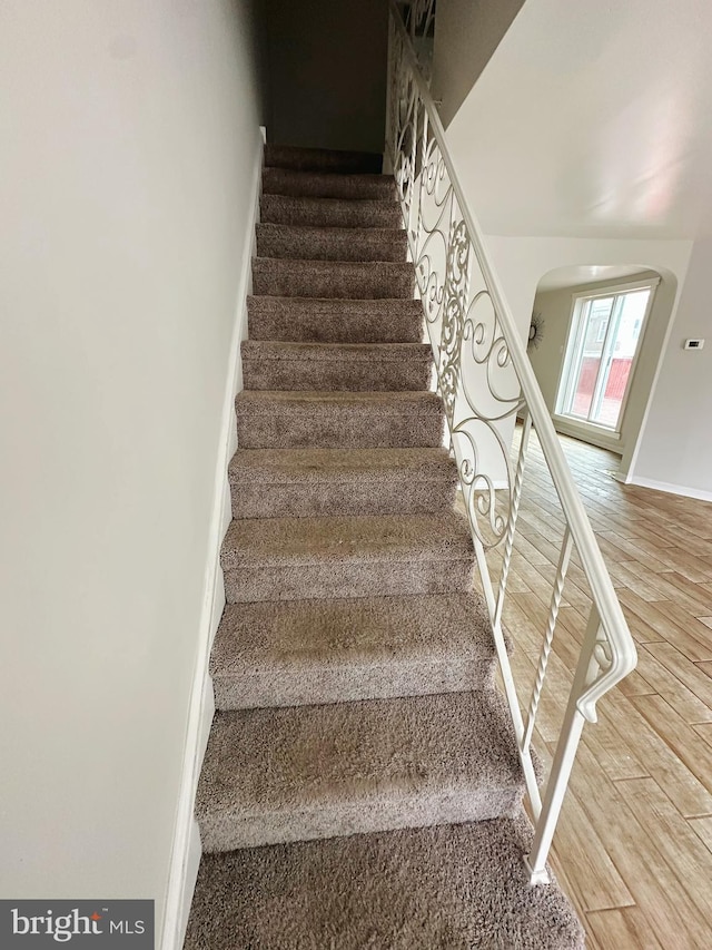 stairs featuring wood finished floors, baseboards, and arched walkways