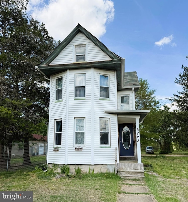 victorian home featuring entry steps, fence, and a front lawn
