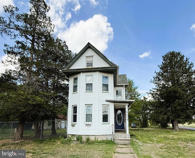 victorian-style house featuring entry steps, fence, and a front lawn