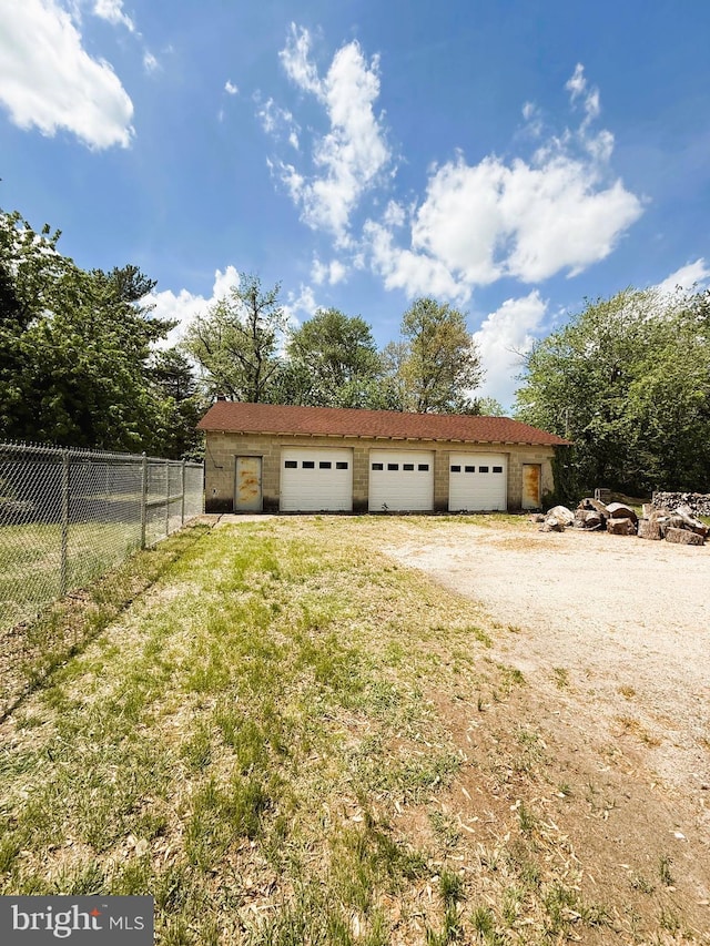 detached garage featuring dirt driveway and fence