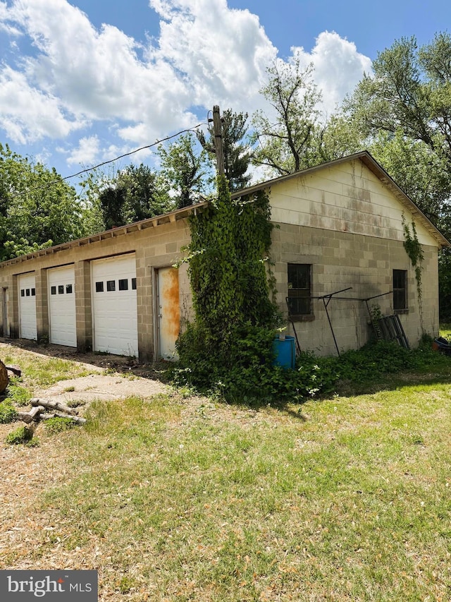 view of side of property with a yard, a detached garage, and concrete block siding