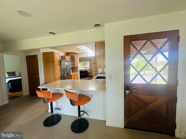 481 Laudermilch Rd, Hershey, PA 17033 - kitchen with stainless steel fridge, brown cabinetry, a breakfast bar, glass insert cabinets, and light countertops