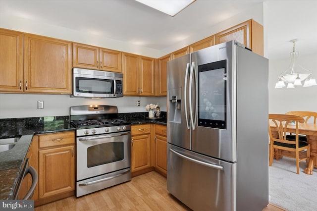 kitchen featuring stainless steel appliances, dark stone countertops, a chandelier, and light wood-style flooring