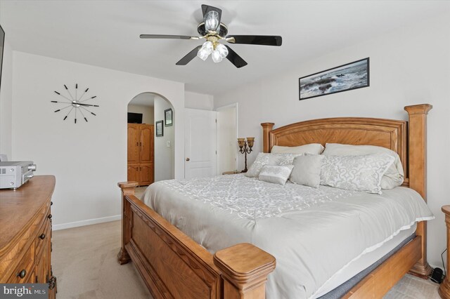 bedroom featuring light colored carpet, arched walkways, baseboards, and a ceiling fan