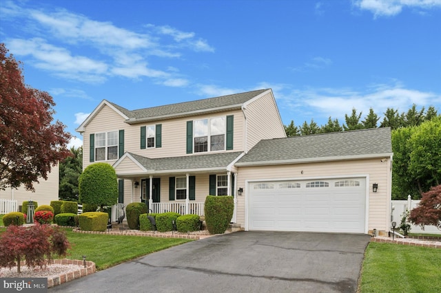 traditional home with covered porch, asphalt driveway, an attached garage, a front yard, and a shingled roof