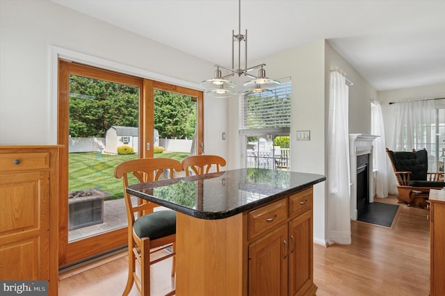 kitchen featuring light wood finished floors, a kitchen bar, decorative light fixtures, a fireplace with flush hearth, and a kitchen island