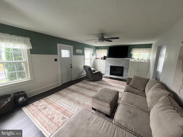 living room featuring wood finished floors, a ceiling fan, a fireplace, a textured ceiling, and baseboards