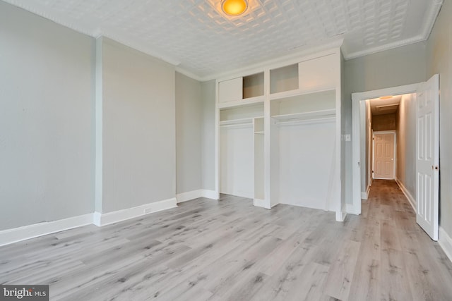 unfurnished bedroom with ornamental molding, a closet, light wood-type flooring, and baseboards
