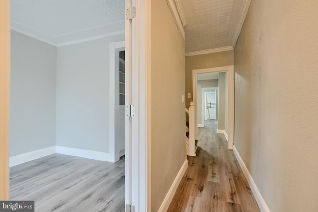 hallway featuring wood finished floors, ornamental molding, a textured wall, and baseboards