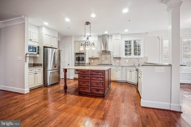 kitchen with a kitchen bar, baseboards, wall chimney range hood, appliances with stainless steel finishes, and decorative backsplash