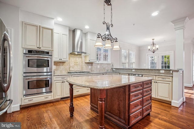 kitchen featuring wall chimney range hood, appliances with stainless steel finishes, dark wood-style floors, and a breakfast bar