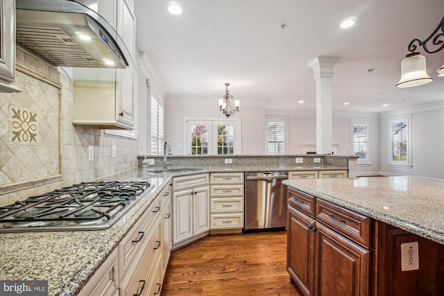 kitchen featuring a healthy amount of sunlight, a sink, crown molding, wall chimney range hood, and stainless steel appliances