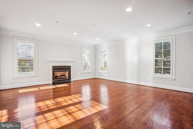 unfurnished living room featuring a premium fireplace, ornamental molding, baseboards, and wood finished floors
