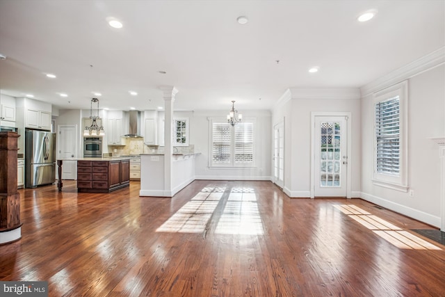 unfurnished living room featuring an inviting chandelier, ornamental molding, plenty of natural light, and recessed lighting