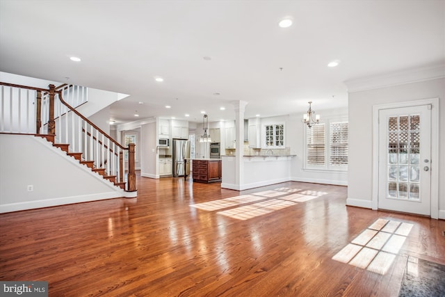 unfurnished living room with wood finished floors, crown molding, baseboards, a chandelier, and recessed lighting