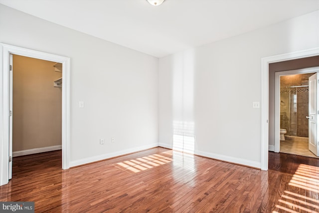 unfurnished bedroom with baseboards, a closet, wood finished floors, and a walk in closet