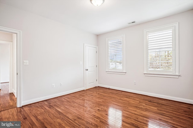 unfurnished room featuring baseboards, visible vents, and wood finished floors