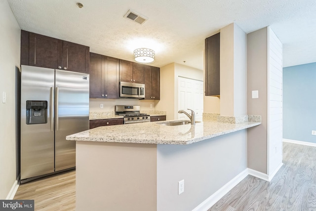 kitchen with appliances with stainless steel finishes, a sink, light wood-style flooring, dark brown cabinetry, and a textured ceiling