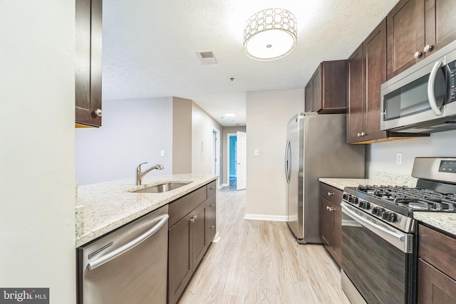 kitchen featuring light wood-style floors, appliances with stainless steel finishes, dark brown cabinets, and a sink