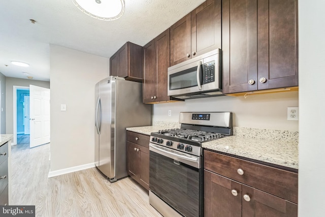 kitchen with dark brown cabinets, baseboards, light stone counters, light wood-style floors, and stainless steel appliances