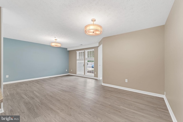 empty room with a textured ceiling, baseboards, and wood finished floors
