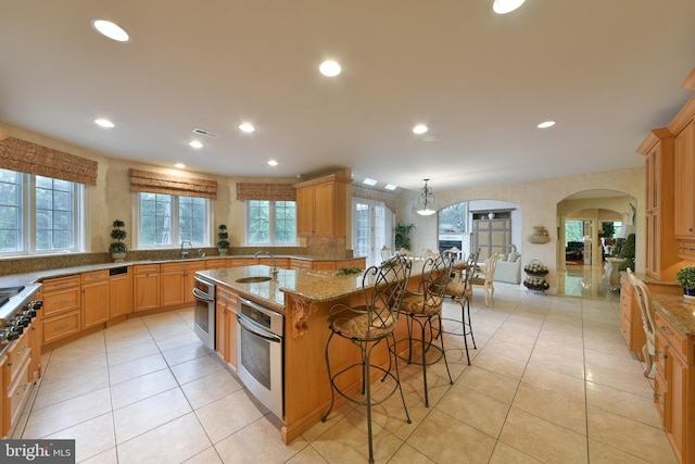 1389 Lamplighter Cir, Gwynedd, PA 19436 - kitchen with appliances with stainless steel finishes, arched walkways, a breakfast bar area, a sink, and light stone countertops