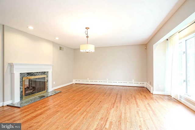 unfurnished living room with wood finished floors, a premium fireplace, healthy amount of natural light, a baseboard radiator, and recessed lighting
