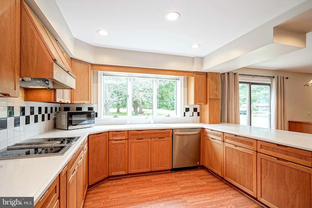 kitchen with appliances with stainless steel finishes, premium range hood, light countertops, backsplash, and light wood-style floors