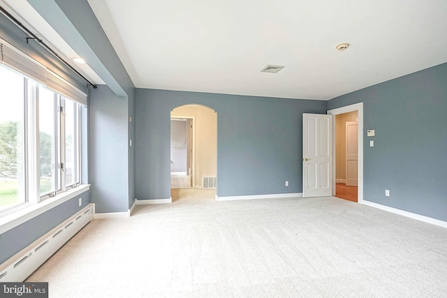 carpeted spare room featuring baseboard heating, arched walkways, and baseboards